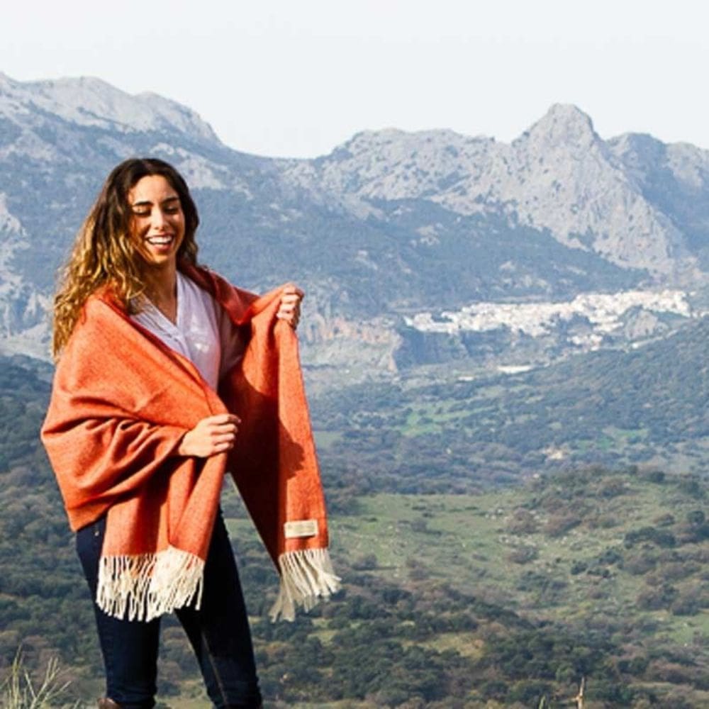 Fotomodel met bergen op de achtergrond. Zij draagt de donker oranje merino stola